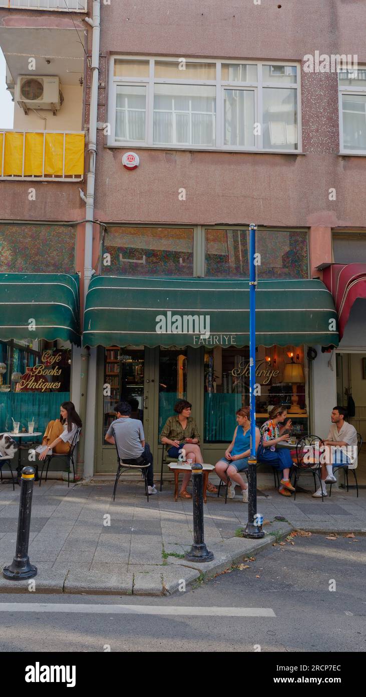 Gente socializando fuera de una cafetería y librería debajo de las casas en el barrio de Kadikoy en el lado asiático de Estambul, Turquía Foto de stock