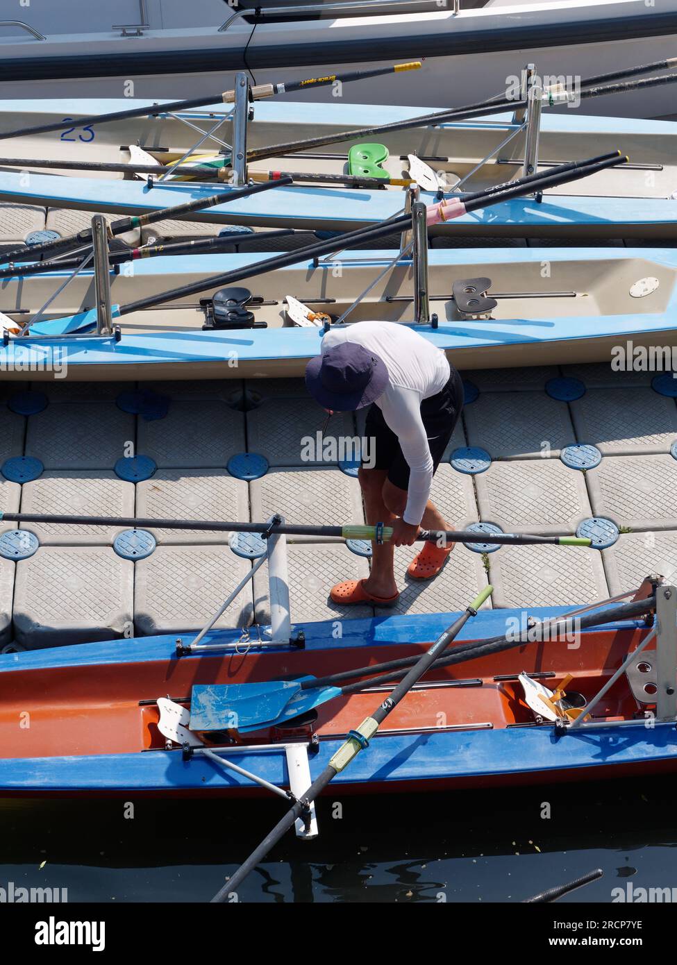 Vista de arriba abajo de un hombre con sombrero negro se inclina hacia abajo para recoger un remo entre los barcos de remo. Anadolu en el lado asiático de Estambul, Turquía Foto de stock