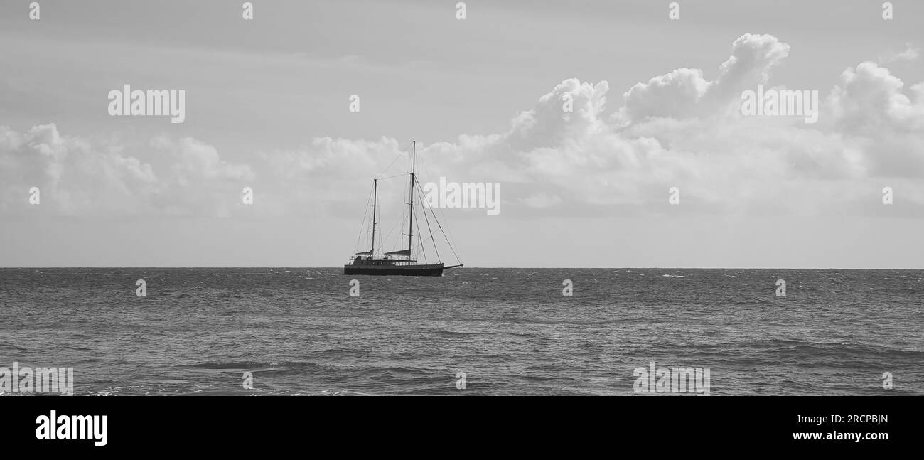 Blanco y negro de paso del barco de vela cerca de la orilla del punto noreste de Mahe, Seychelles Foto de stock