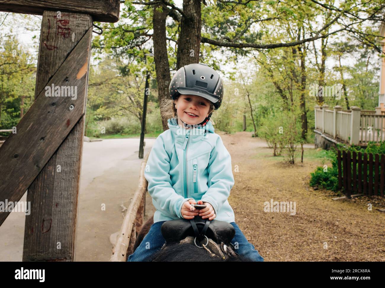 chica de 4 años sonriendo mientras monta un caballo en el bosque Foto de stock