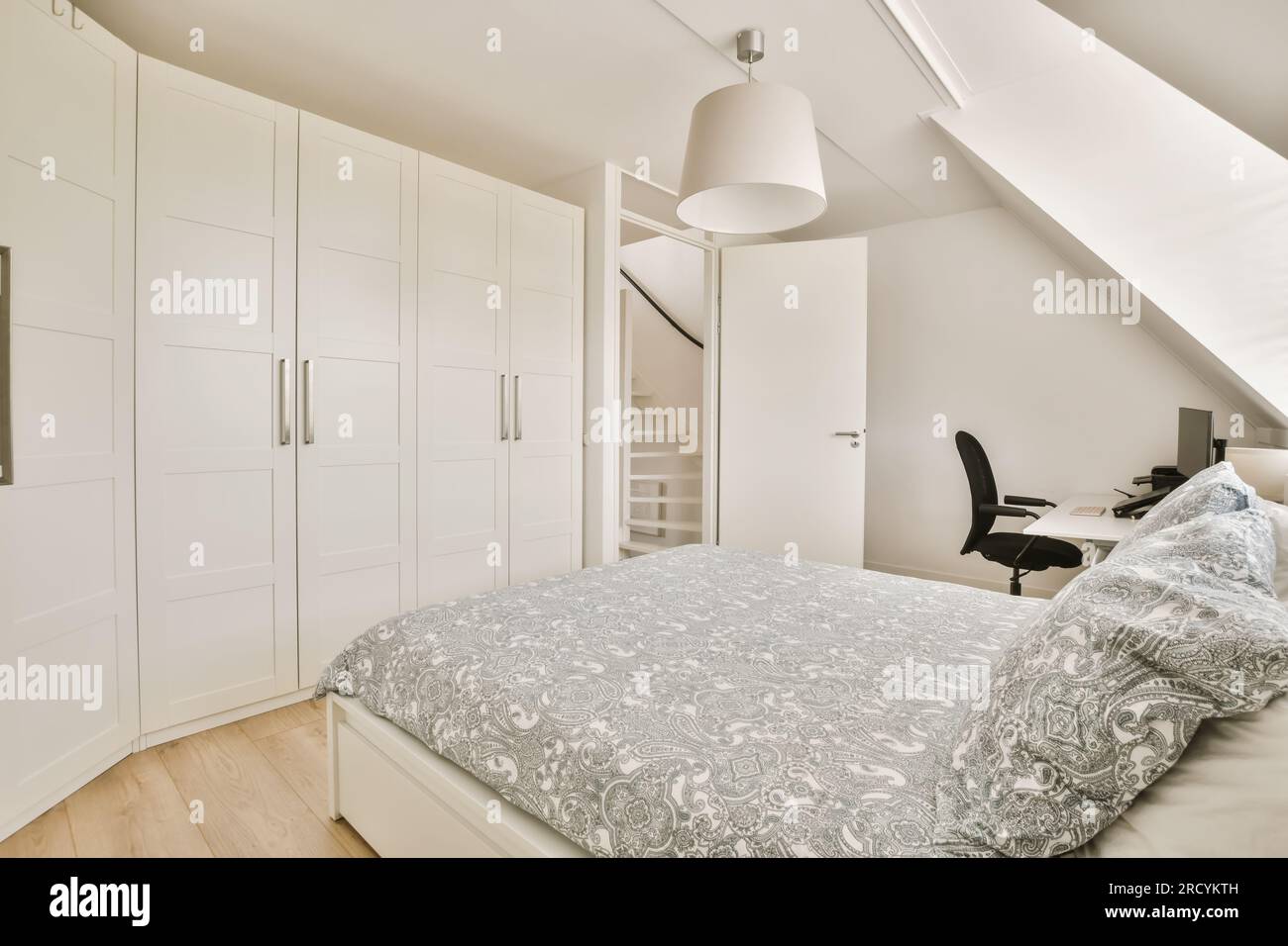 un dormitorio con una cama, escritorio y armarios en la pared al lado es un  armario de cabinetd blanco Fotografía de stock - Alamy