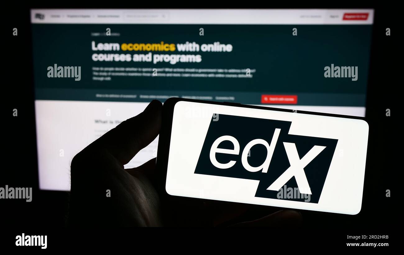 Persona que sostiene el teléfono inteligente con el logotipo de la compañía estadounidense de e-learning edX LLC en la pantalla frente al sitio web. Enfoque en la pantalla del teléfono. Foto de stock