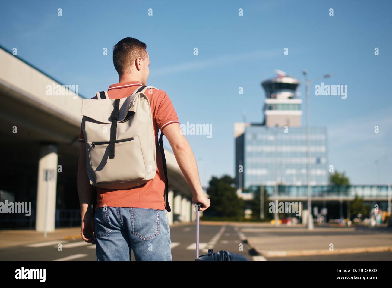 Viaje en avión. El viajero está caminando a la terminal del aeropuerto. Hombre con maleta contra la torre de control de tráfico aéreo. Foto de stock