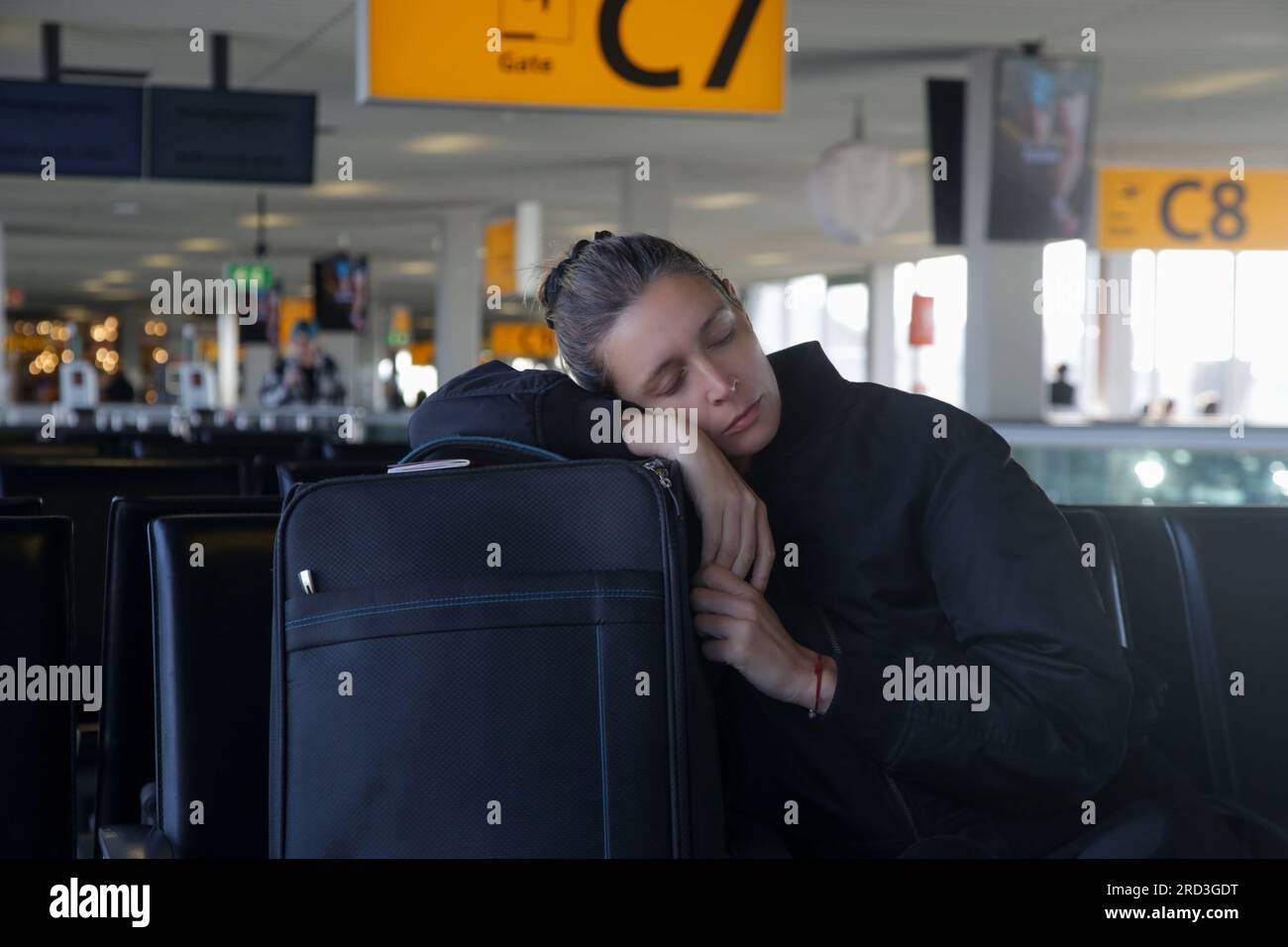 Mujer turística cansada que duerme en el equipaje mientras espera su vuelo en la terminal del aeropuerto Foto de stock