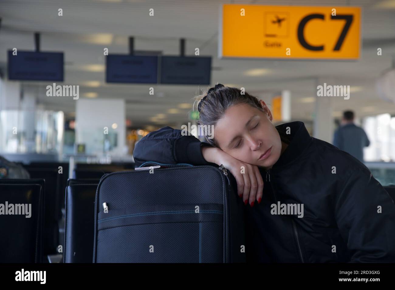 Mujer turística cansada que duerme en el equipaje mientras espera su vuelo en la terminal del aeropuerto Foto de stock