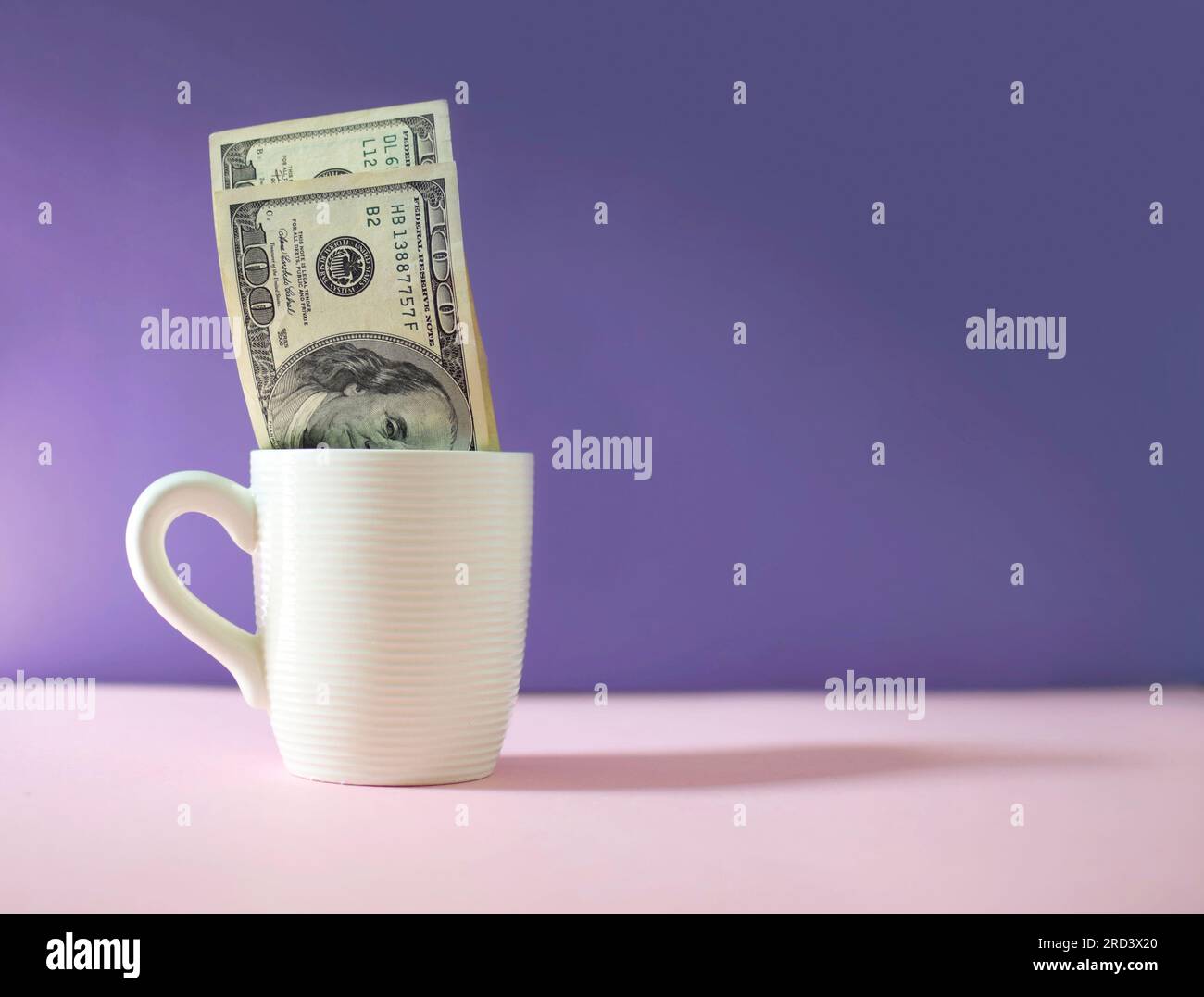 Billetes de dólar en una taza de café con fondo púrpura. Moneda/finanzas Foto de stock