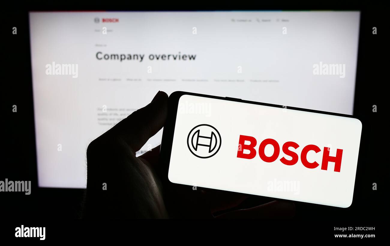 Persona que sostiene el teléfono inteligente con el logotipo de la empresa de ingeniería alemana Robert Bosch GmbH en la pantalla delante del sitio web. Enfoque en la pantalla del teléfono. Foto de stock