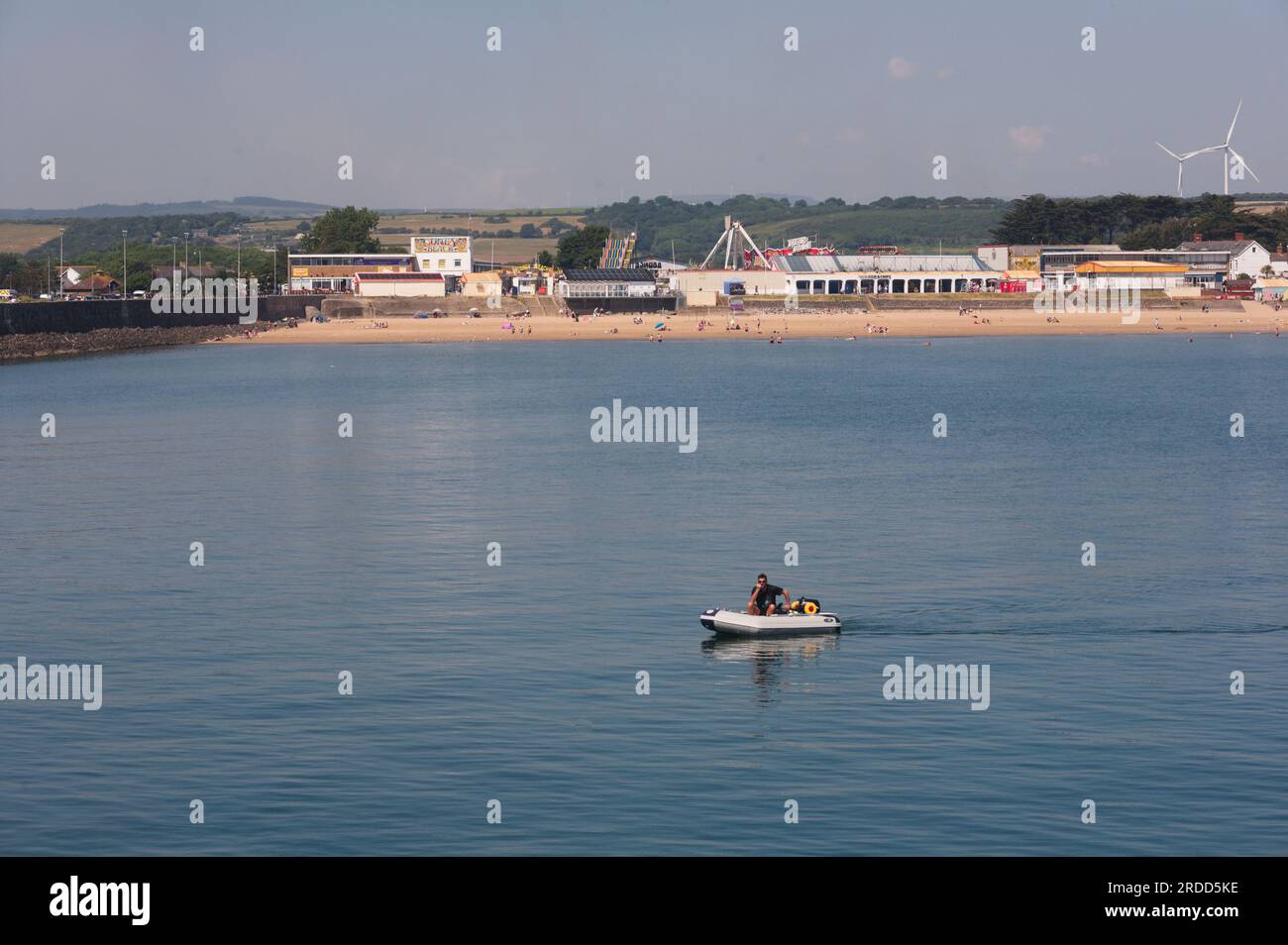 Sandy Bay Porthcwal con diversiones de Coney Beach y hombre en bote en la tranquila y cálida tarde de junio Foto de stock