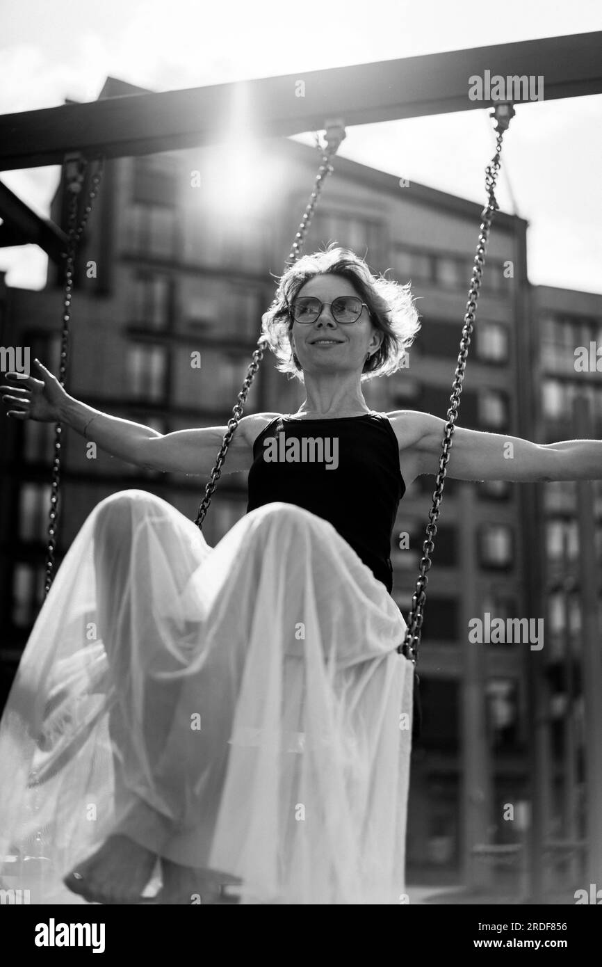 Una mujer se balancea en un columpio, ambiente de verano. Foto de stock