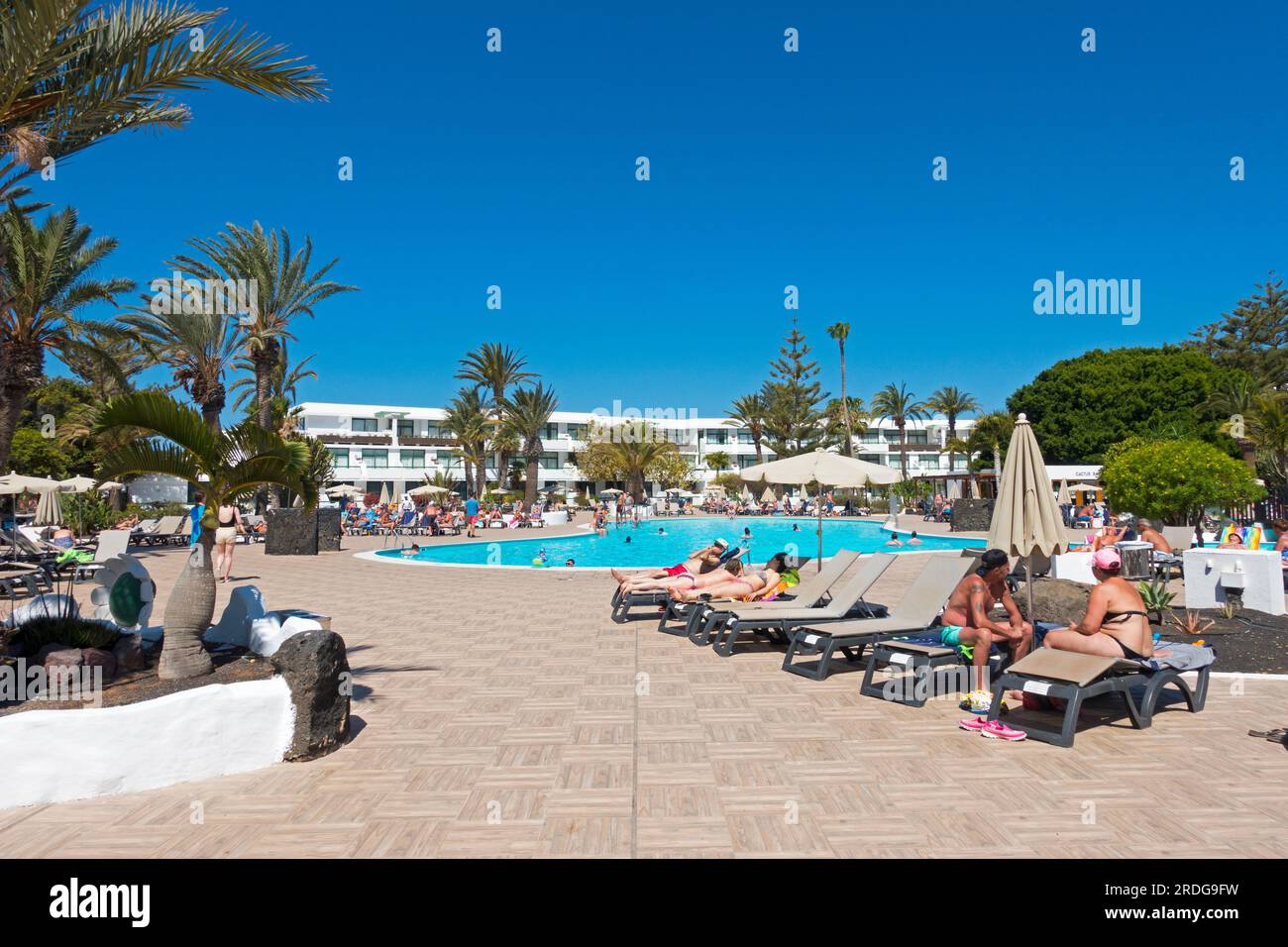 Vista típica de los huéspedes tomando el sol alrededor de una piscina en un hotel resort en la isla de Lanzarote, Islas Canarias, España Foto de stock