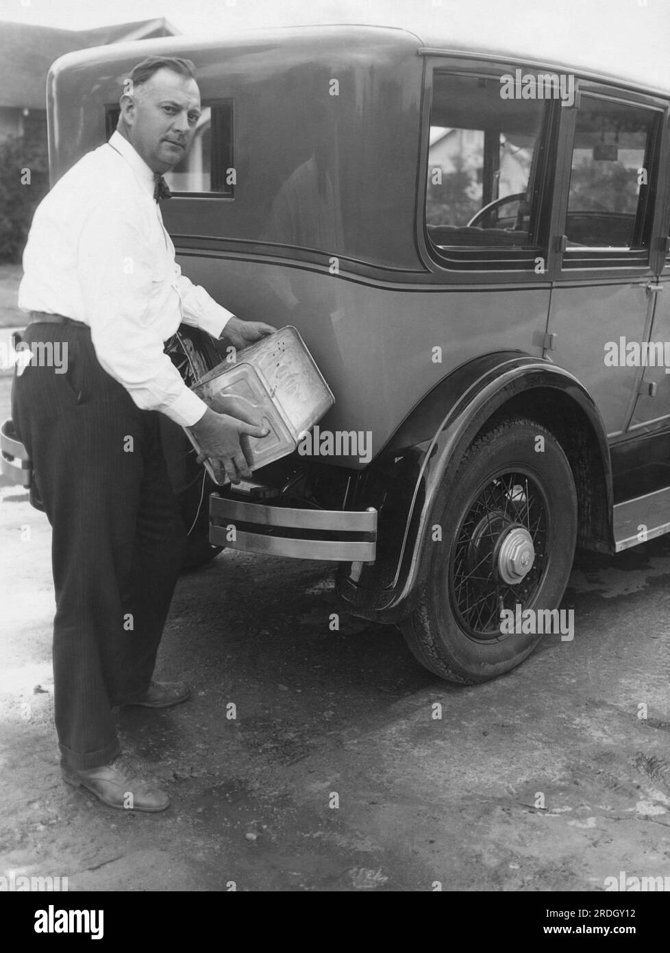 Los Ángeles, California: c. 1926 El químico Daniel Hoge vierte parte de su combustible recién descubierto en su automóvil. El sustituto de la gasolina está hecho de compuestos vegetales por un centavo y medio por galón y es un tercio más potente que el gas de prueba alto. Foto de stock