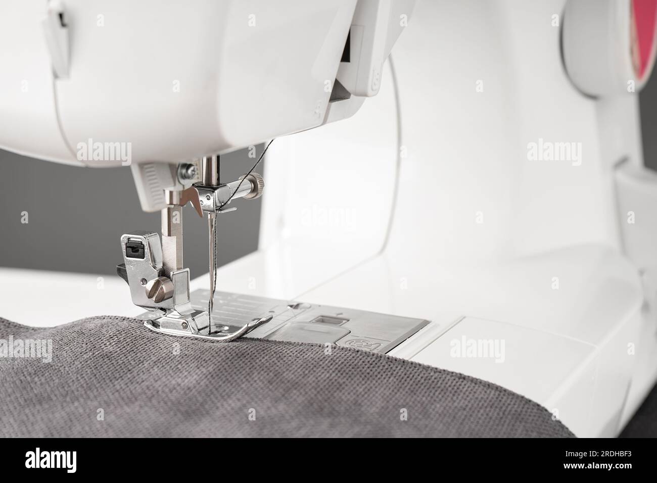 Máquina de coser moderna con tela gris y. Proceso de costura ropa, cortinas, tapicería. Negocio, hobby, hecho a mano, cero residuos, reciclaje, reparar con Foto de stock