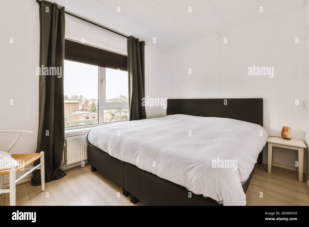 un dormitorio con paredes blancas y cortinas negras en la ventana