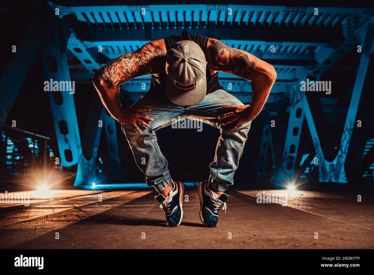 Joven hombre fresco romper bailarín posando en puente urbano en la noche, tatuaje en el cuerpo Foto de stock