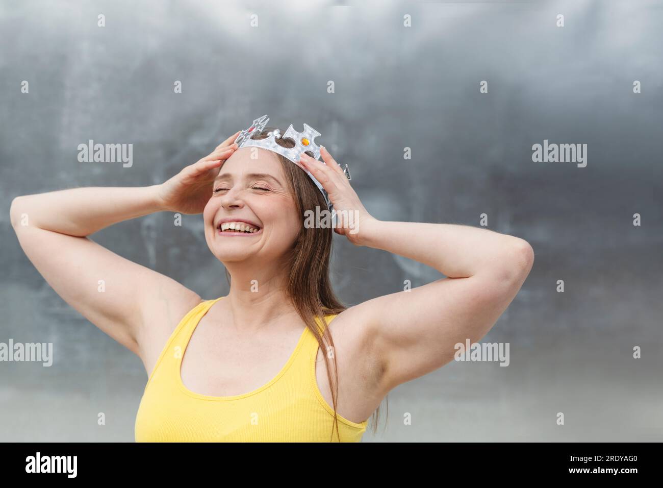 Mujer feliz que lleva la corona delante de la pared Foto de stock