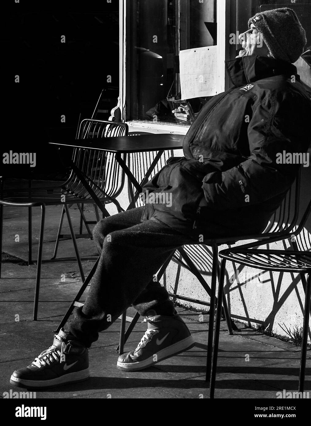 hombre viejo en la calle de café sentado tomando el sol en la luz del sol del invierno Foto de stock