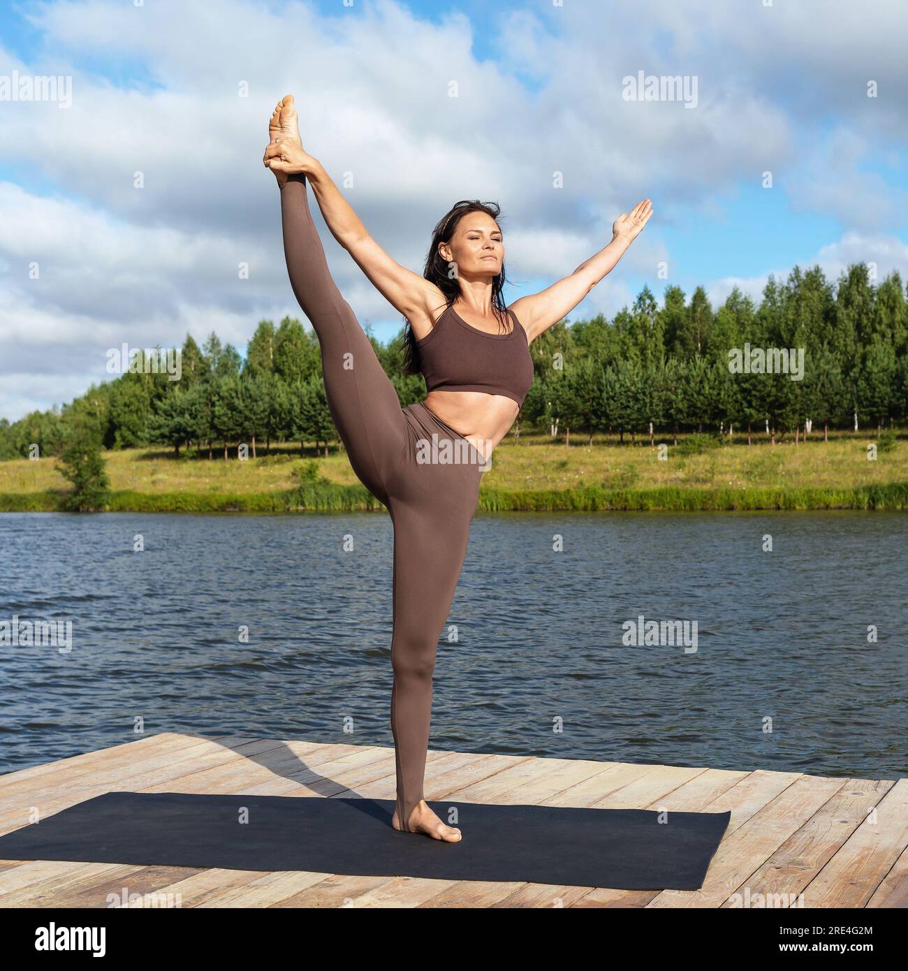 Mujer practicante de yoga, realiza ejercicio Utthita Hasta Padangushthasana, equilibrio en una pierna, entrena en ropa deportiva de pie en el puente de madera en los lagos Foto de stock