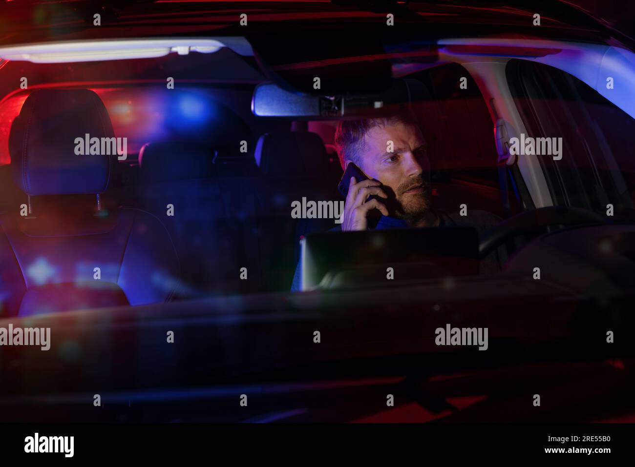 hombre sentado dentro de un coche y hablando por teléfono después de ser detenido por la policía en la noche Foto de stock