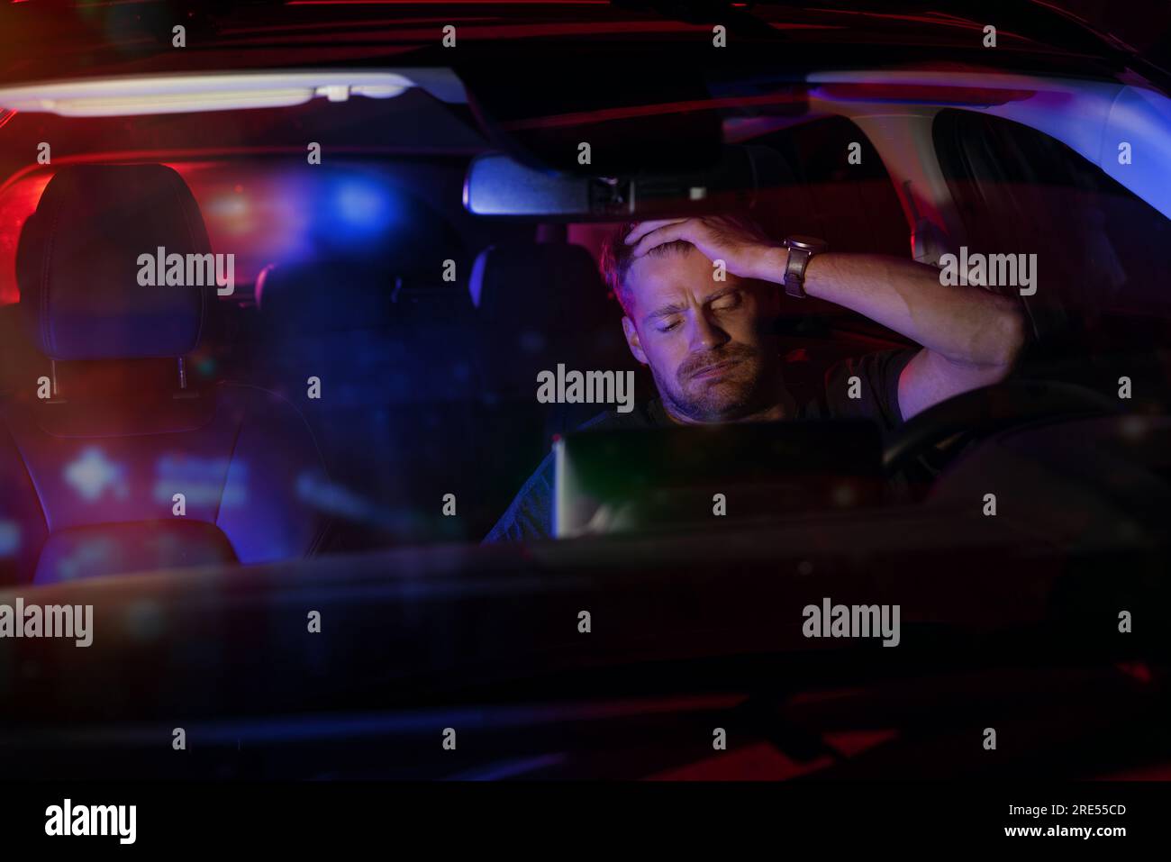hombre desesperado sentado dentro de un coche después de ser detenido por la policía por violaciones de tráfico en la carretera por la noche Foto de stock