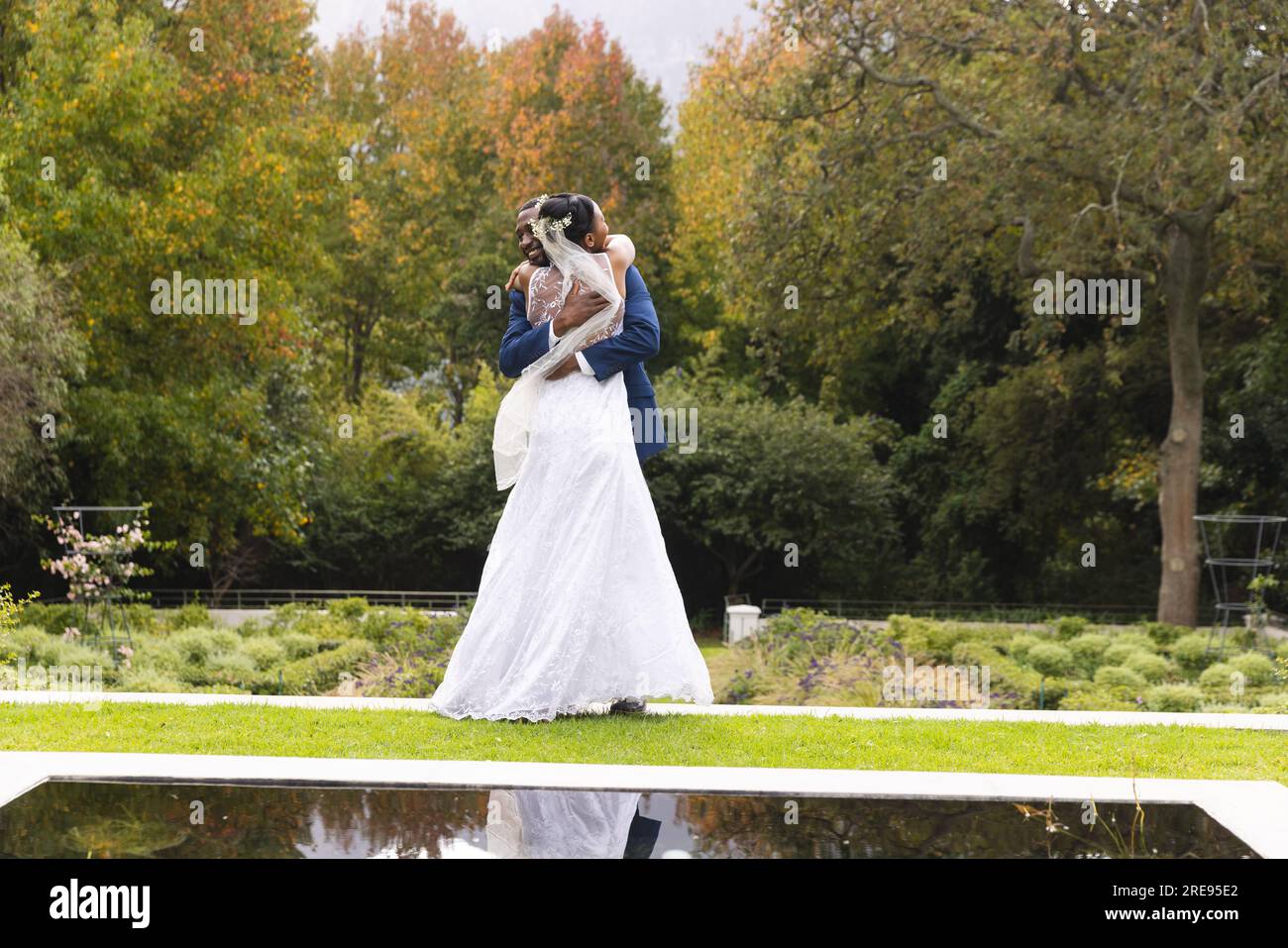 Feliz novia y novio afroamericano abrazando el día de la boda en jardín soleado, espacio de copia Foto de stock