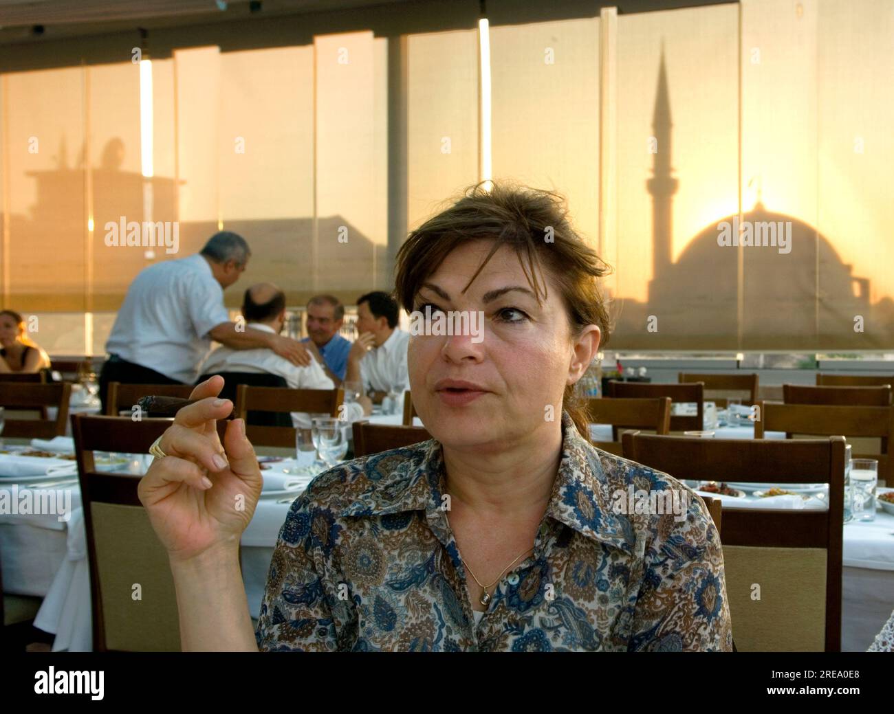 Una mujer turca moderna fumando un cigarrillo en un restaurante con una mezquita visible a través de sombras dibujadas al atardecer en Estambul, Turquía Foto de stock