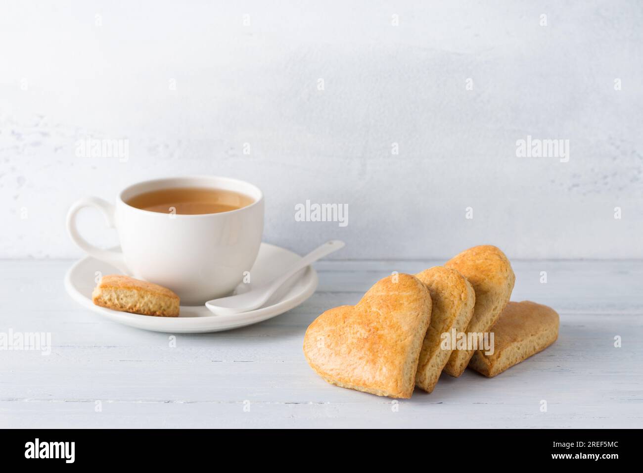 Galletas de shortbread en forma de corazón con una taza de té sobre un fondo azul claro. día de la cookie. Foto de stock