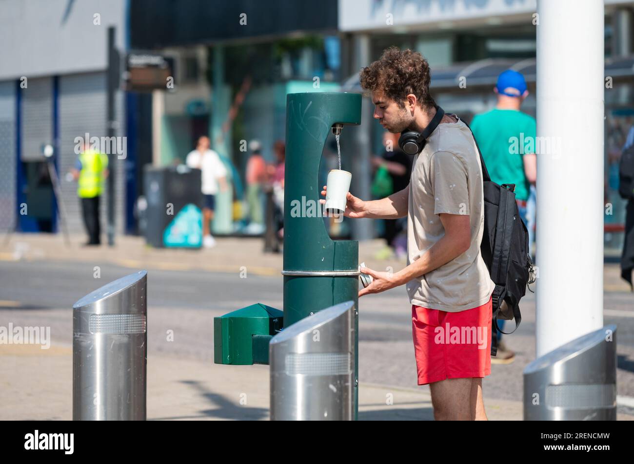 Joven llenando una taza con agua de un dispensador de agua público o fuente de agua potable Verano en Brighton, Brighton & Hove, Inglaterra, Reino Unido. Foto de stock