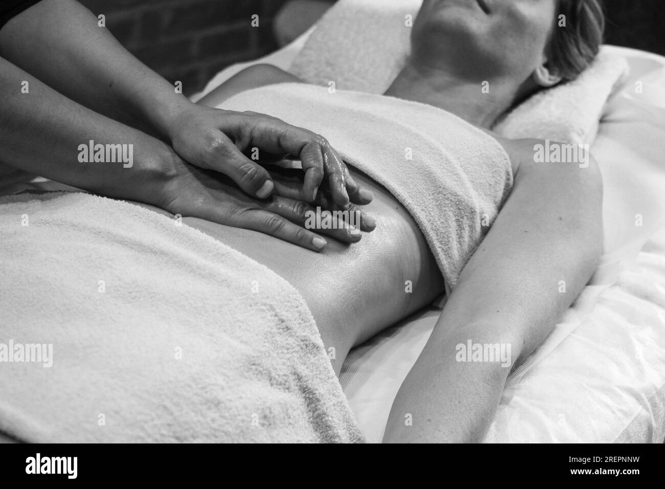 Cierre las manos del quiropráctico o masajista que hace un masaje abdominal relajante a una mujer joven en forma acostada en la cabina del spa de bienestar. Foto de stock