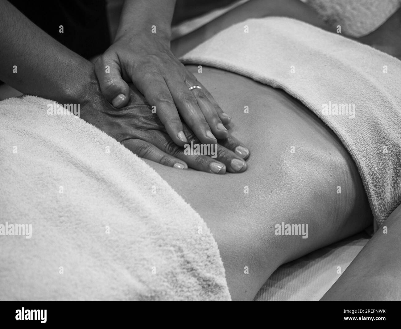 Cierre las manos del quiropráctico o masajista que hace un masaje abdominal relajante a una mujer joven en forma acostada en la cabina del spa de bienestar. Foto de stock