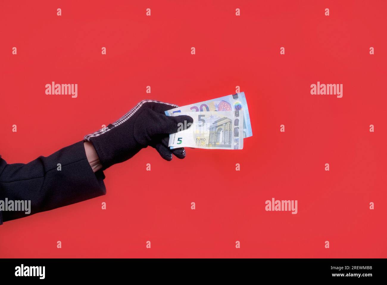 Billetes de euro en una mano femenina en un guante. Sobre un fondo rojo. cinco y veinte euros Foto de stock
