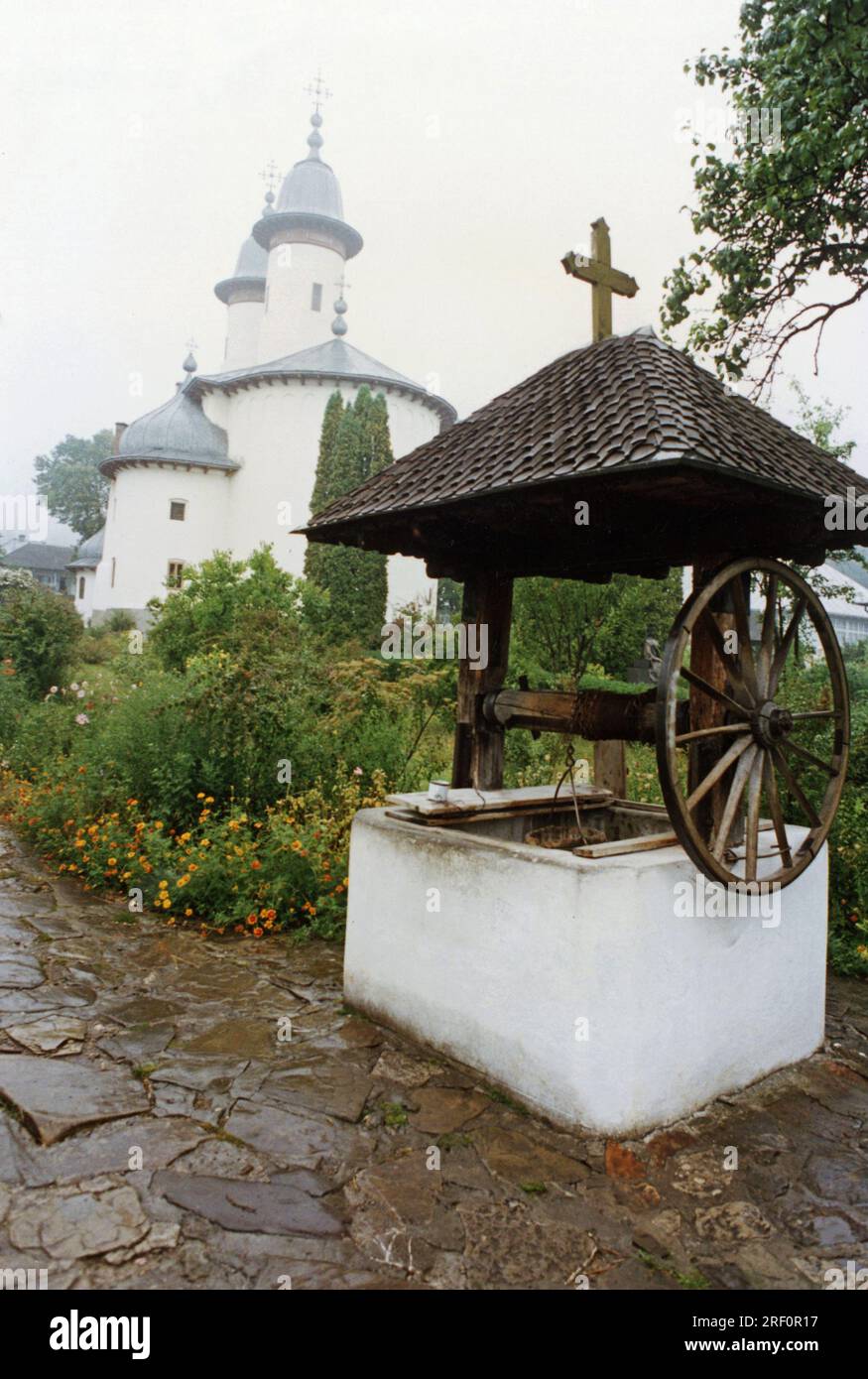 Condado de Neamt, Rumania, 1999. Un pozo de agua en los terrenos del Monasterio de Varatec, con la iglesia 'Dormición de la Virgen María' en la parte posterior. Foto de stock