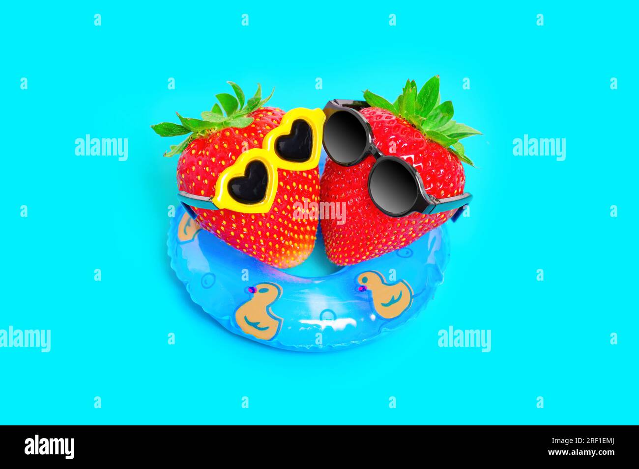 Vista de arriba hacia abajo de dos fresas, con gafas de sol elegantes, flotando en un flotador inflable. Vibrante concepto de escapada de verano de ensueño. Foto de stock