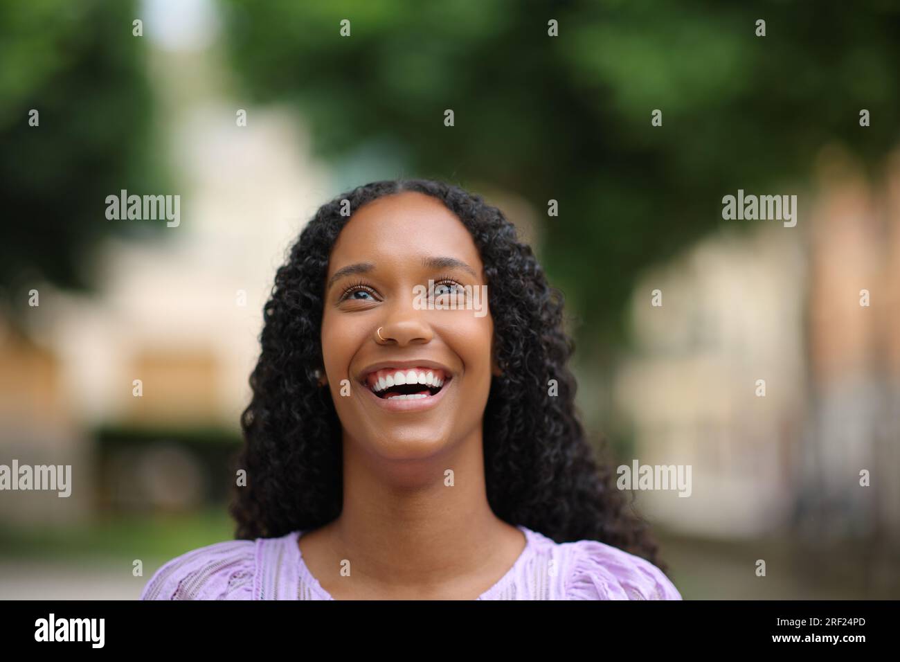 Retrato de vista frontal de una mujer negra riendo mirando hacia arriba con dientes blancos en la calle Foto de stock