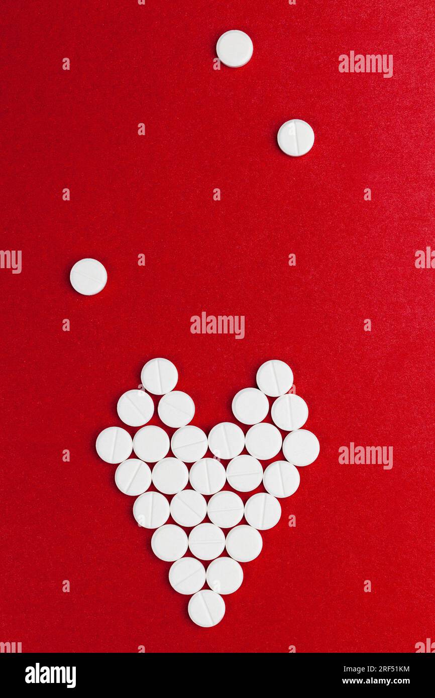 un símbolo del corazón, hecho de medicamentos esenciales, un concepto de tratamiento en cardiología, tabletas de medicamentos médicos apilados en un fondo rojo en forma de Foto de stock