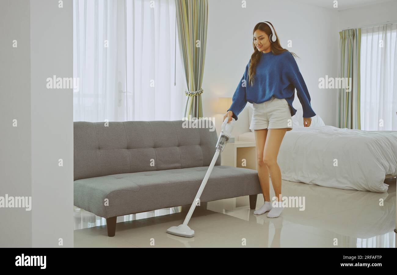 Mujer joven que sostiene la aspiradora, cantando y limpiando en su dormitorio. Foto de stock