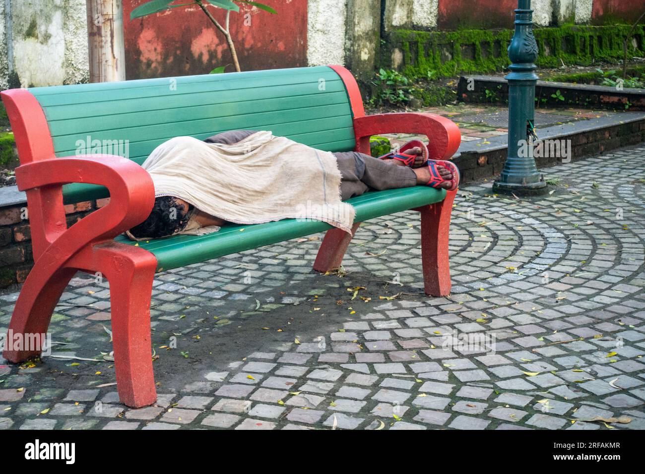 Oct.14th 2022 Uttarakhand, India. Hombre sin hogar vulnerable que encuentra refugio en un banco del parque, envuelto en una manta. Conmovedora representación de la falta de vivienda AN Foto de stock