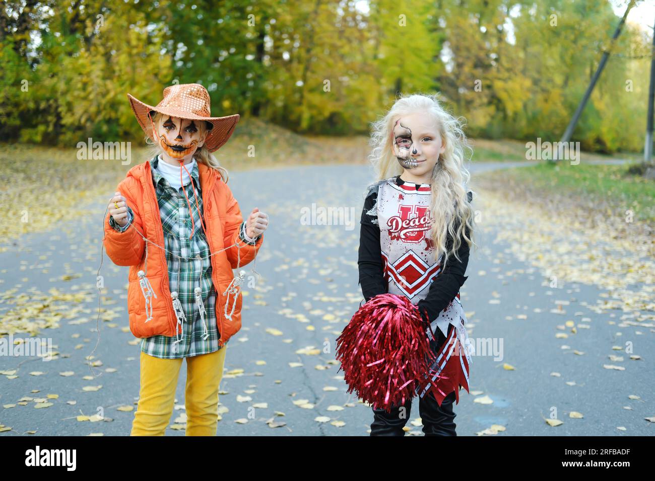 Una chica con un disfraz de animadora con maquillaje de esqueleto de media  cara y una chica con maquillaje de calabaza