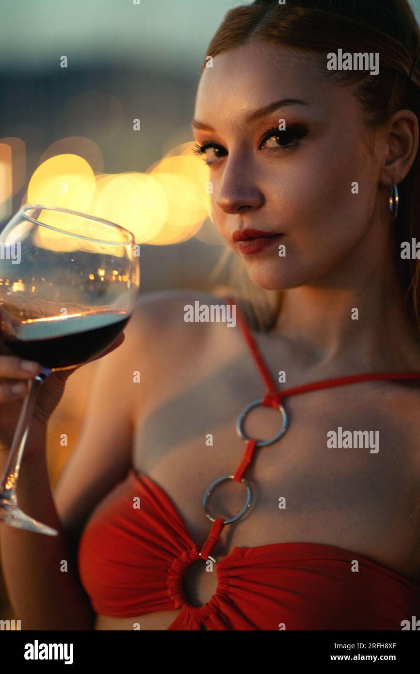 Un retrato de cerca de una joven de veinte años con un vestido naranja, sosteniendo una copa llena de vino tinto Foto de stock