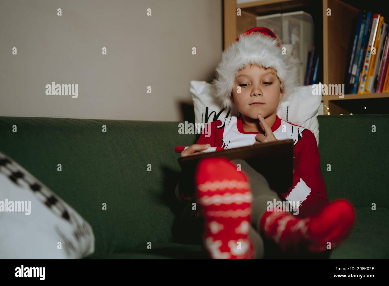 Niño pequeño en camiseta de santa y sombrero escribiendo carta a Santa  Claus sentado en el sofá mordiendo la pluma de fieltro. Imagen con enfoque  selectivo Fotografía de stock - Alamy
