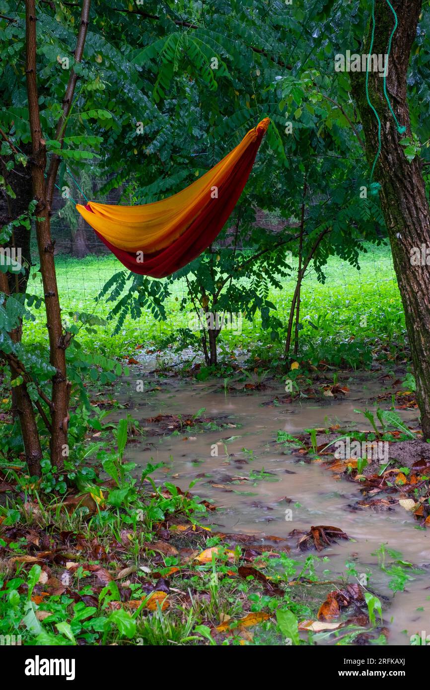 hamaca empapada que cuelga despreciadamente en el jardín empapado de la lluvia sobre la corriente de agua simbólica del lavado de verano típico del condado de zala hungría Foto de stock