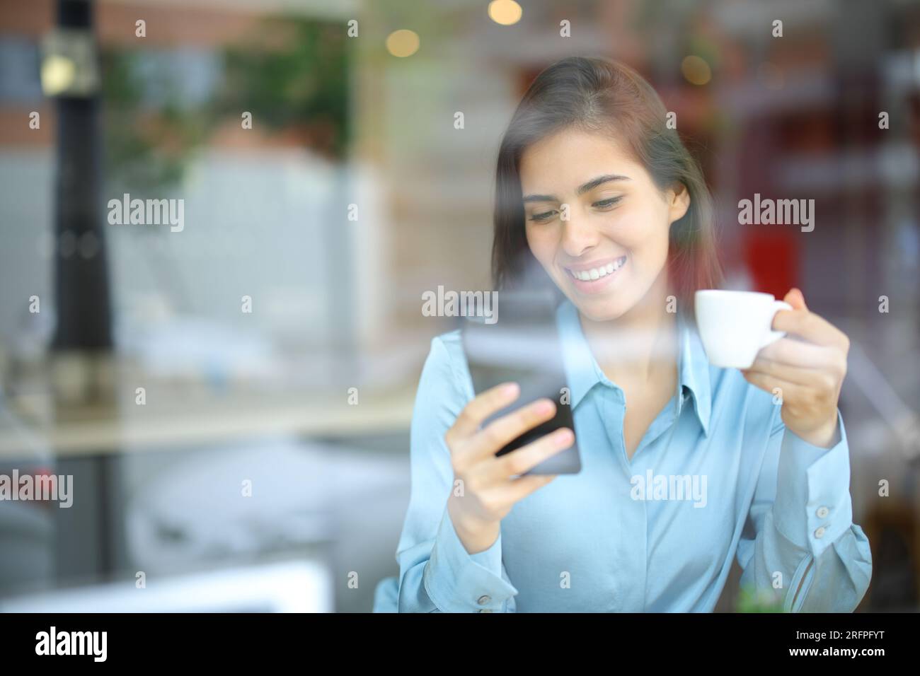 Mujer feliz bebiendo y usando teléfono inteligente en un interior de bar Foto de stock