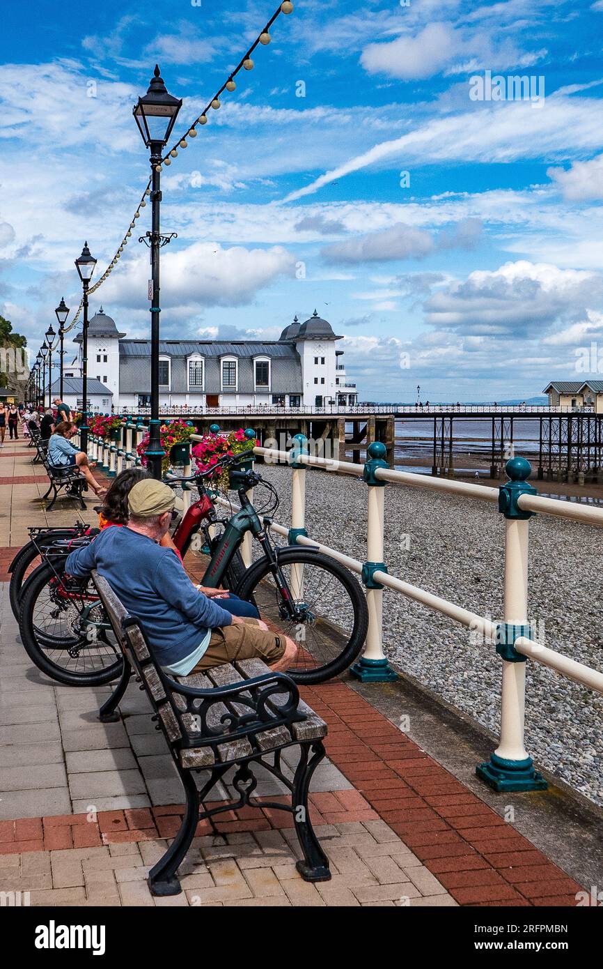 Pareja sentada junto a sus bicicletas en un paseo marítimo en un día de verano. Pier en el fondo. Día soleado. Concepto relajante. Foto de stock