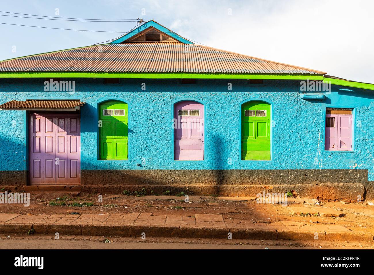 Almacén con pared enlucida azul, puertas y ventanas rosa y verde. Colores llamativos. Foto de stock