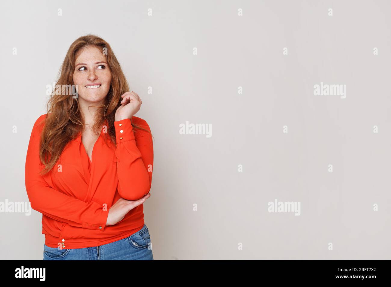 Mujer alegre en ropa casual pensando mirando hacia arriba y de pie contra el fondo blanco de la pared del estudio Foto de stock