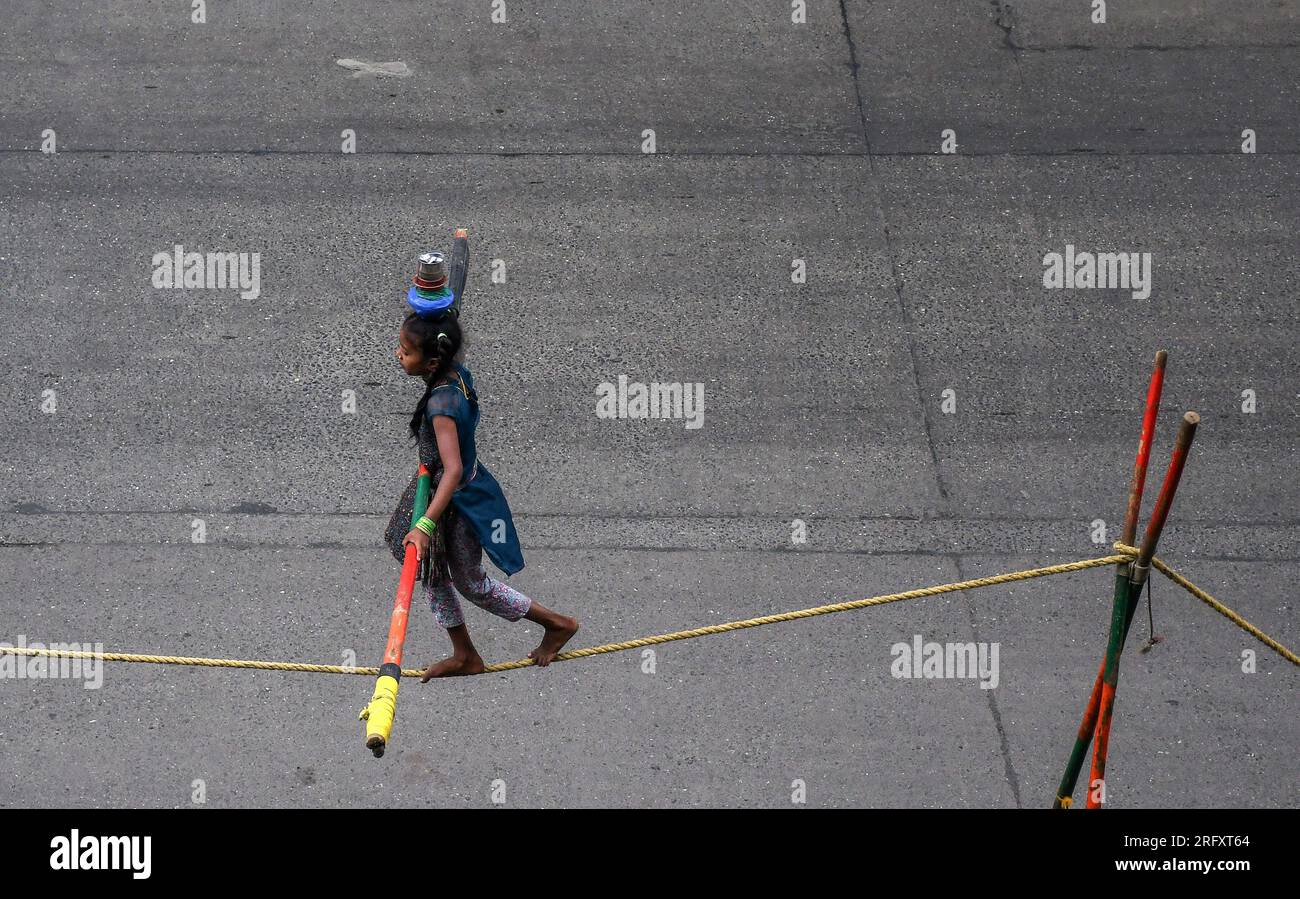 Mumbai, India. 06 de agosto de 2023. Una niña sosteniendo un palo de bambú para equilibrarse realiza un paseo por la cuerda floja en la calle de Mumbai. Los caminantes de cuerda floja se ganan su sustento actuando en las calles dependiendo principalmente del dinero dado por la gente que observa su acto de riesgo. (Foto por Ashish Vaishnav/SOPA Images/Sipa USA) Crédito: SIPA USA/Alamy Live News Crédito: SIPA USA/Alamy Live News Foto de stock
