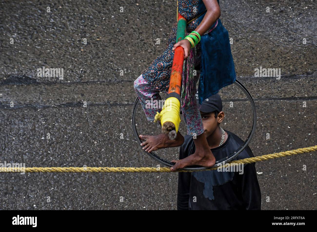 Mumbai, India. 06 de agosto de 2023. Una niña sosteniendo un palo de bambú y un anillo de metal circular para equilibrarse realiza un paseo por la cuerda floja en la calle de Mumbai. Los caminantes de cuerda floja se ganan su sustento actuando en las calles dependiendo principalmente del dinero dado por la gente que observa su acto de riesgo. (Foto por Ashish Vaishnav/SOPA Images/Sipa USA) Crédito: SIPA USA/Alamy Live News Crédito: SIPA USA/Alamy Live News Foto de stock