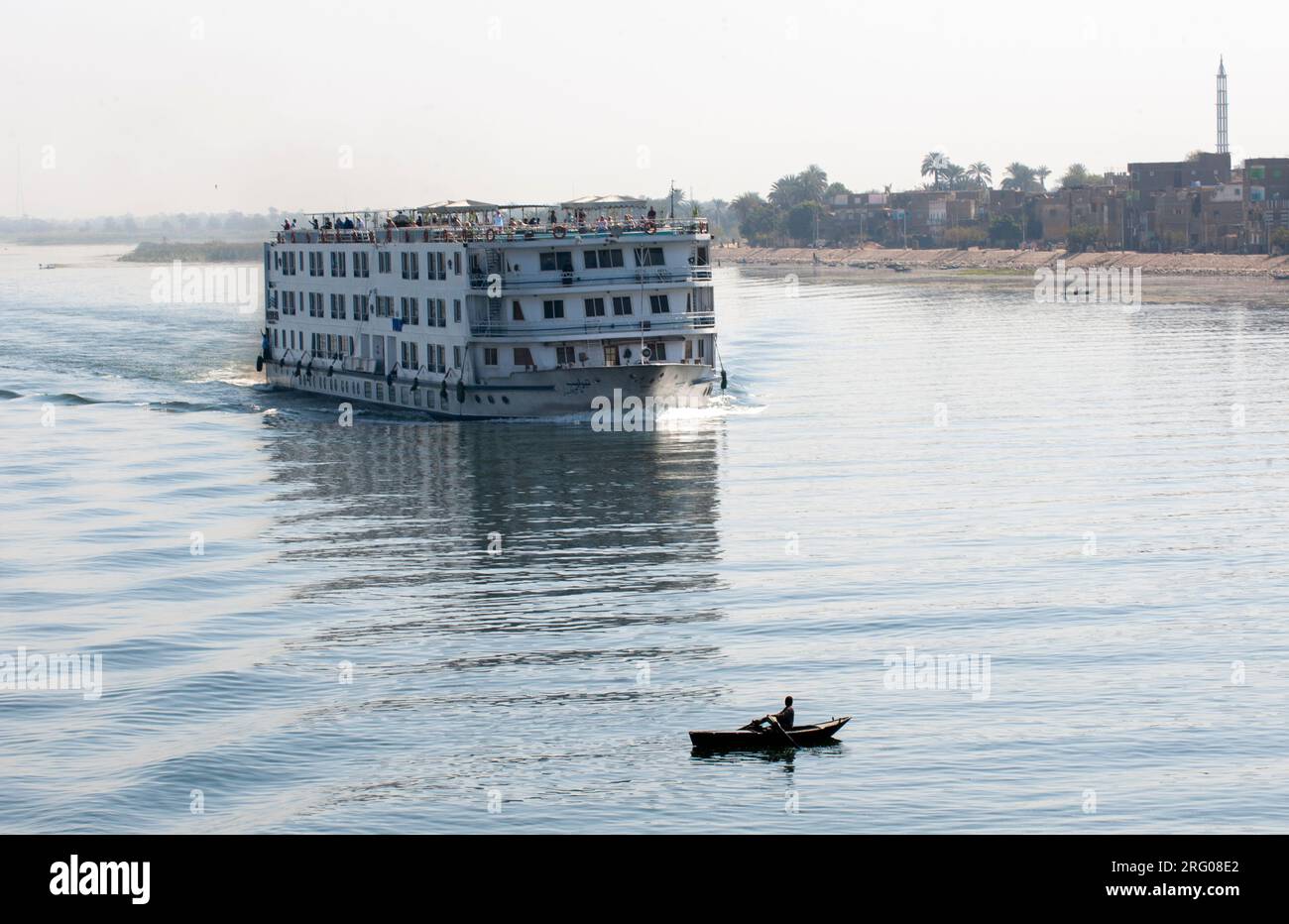 África, Egipto, río Nilo. Yuxtaposición entre un pequeño bote de remo y un gran crucero de pasajeros en el río Nilo. Foto de stock