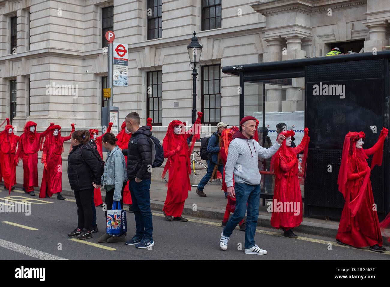 Londres, Reino Unido, 2023. Frente a la parada de autobús de Whitehall, los turistas observan la Brigada Rebelde Roja de la Rebelión de Extinción marchando hacia Westminster Foto de stock