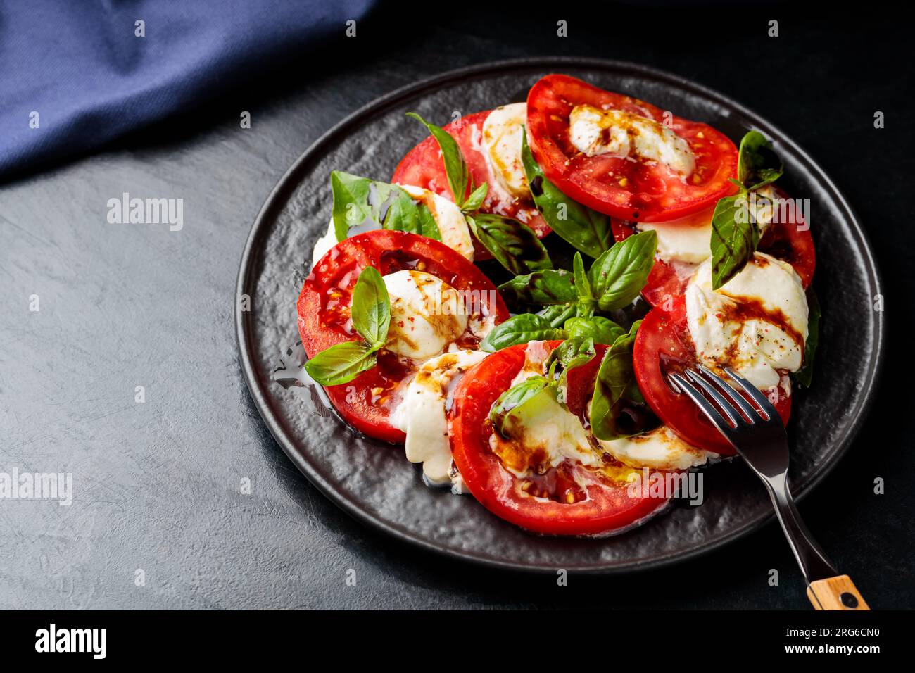 Ensalada Caprese. Rodajas de tomate y mozzarella con hojas de albahaca con tenedor en plato oscuro. Comida tradicional italiana Foto de stock