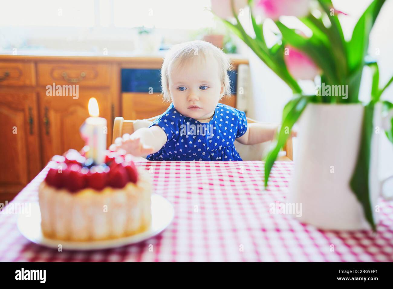 Bebé feliz en vestido azul celebrando su primer cumpleaños. Niño pequeño con pastel de cumpleaños y vela Foto de stock